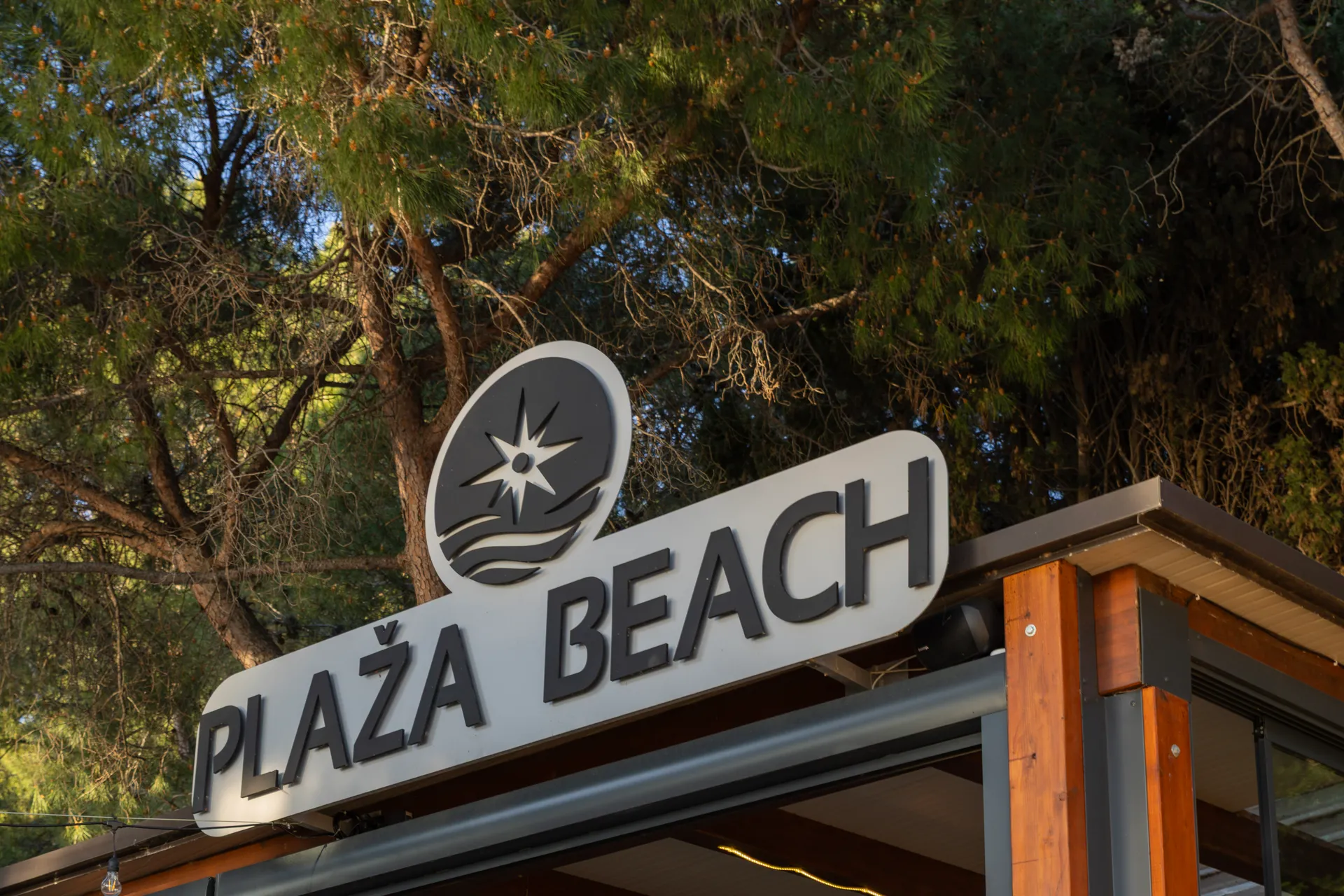 Natpis Plaža Beach iznad ulaza okružen borovima